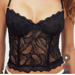 Svart spetsig bustier topp - Snygg svart bustier topp med genomskinlig spets och blommigt mönster. Justerbara axelband och formade kupor för extra stöd. Perfekt att styla till jeans eller kjol.