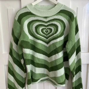 Grön stickad tröja med hjärtmönster från Cider - Säljer en stickad tröja från Cider i grönt och vitt med ett stort hjärtmönster i mitten och breda ränder 💚