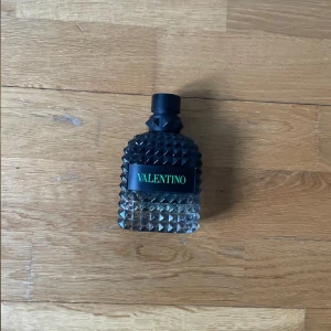 Valentino greenwtarvaganza - Skriv till mig för mer information! Säljer en lyxig parfym från Valentino i en transparent glasflaska med nitar och svart kork. Flaskan har en modern design med grönt Valentino-tryck på framsidan. Perfekt för dig som gillar exklusiva dofter och snygg inredningsdetalj.