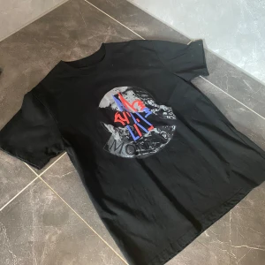 Moncler T-shirt  - Cool svart t-shirt med ett stort grafiskt tryck i rött, blått och grått på bröstet. T-shirten har rund hals och korta ärmar, perfekt för en avslappnad stil. Mer info privat