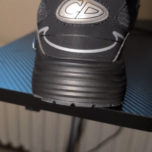 Svarta sneakers  - Säljer ett par svarta sneakers med reflekterande silverdetaljer och CD-logga på hälen. Skorna har snörning, meshpaneler och en robust, mönstrad sula för extra grepp. Perfekta för dig som vill ha en stilren och exklusiv look. Ingen box kommer med.