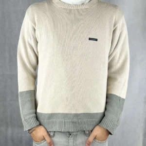 Beige stickad tröja från ysl  - Säljer en stilren beige stickad tröja från ysl med grå ribbade muddar vid ärmslut och nederkant. Tröjan har rund halsringning och en liten logotyp på bröstet. Perfekt för lager-på-lager-stil.