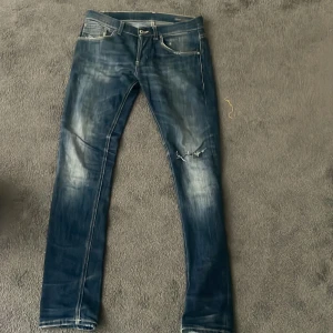 Dondup jeans - Säljer ett par blå dondup jeans med snygga slitningar.Jeansen har en smal passform och är perfekta för dig som gillar en modern stil. Midjan är normal och materialet är klassiskt denim.
