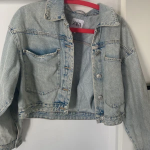Croppad jeansjacka från ZARA - Säljer en ljusblå croppad jeansjacka från ZARA. Jackan har klassisk krage, knappstängning framtill och en stor bröstficka. Perfekt för dig som gillar en avslappnad och trendig stil.