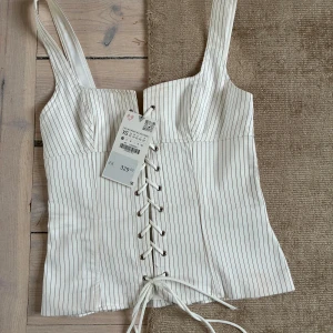  korsettopp - Säljer en vit korsettopp från zara ränder och breda axelband. Toppen har snörning framtill och dragkedja bak. Super snygg!