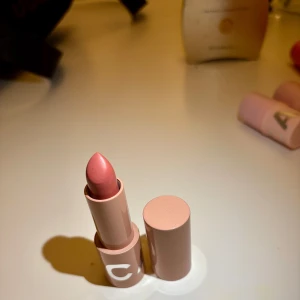 Bestie läppstift från CAIA - Säljer ett läppstift från CAIA i en mjuk ljusrosa nyans. Hylsan är beige med vit text och har en stilren, matt finish. Perfekt för dig som vill ha en naturlig look med lite extra glans.