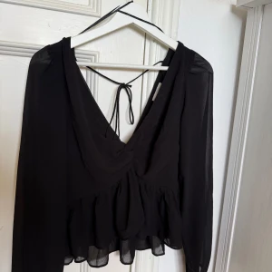 Svart blus med volang och knytband - Säljer en svart blus från H&M med djup v-ringning, volang nertill och knytband i ryggen. Varsamt använd och i mycket bra skick. Kontakta om du har fler frågor 🖤