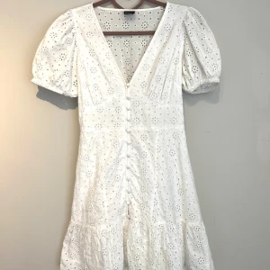 Vit kortklänning med puffärm och broderade detaljer - Superfin vit kortklänning med v-ringning, puffärmar och knappar framtill. Klänningen passar perfekt till både student, konfirmation och midsommar. Använd vid 2 tillfällen så mycket bra skick!🤍 Pris går att diskutera 