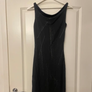 Vintage klänning - Säljer en svart långklänning med glittriga detaljer och asymmetrisk nederkant. Klänningen har en elegant, tight passform och är ärmlös med breda axelband. Ny skick utan prisslapp 