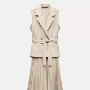 Beige ärmlös klänning med plisserad kjol och bälte - Stilren beige klänning med kavajkrage, dubbelknäppning och knytbälte i midjan. Ärmlös modell med plisserad kjol som ger en elegant siluett. Perfekt för dig som gillar minimalistisk och modern stil.