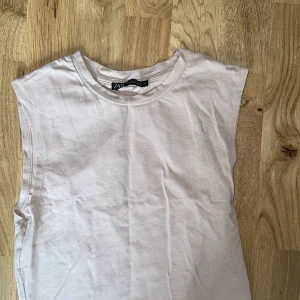 Beige ärmlös topp från Zara - Säljer en enkel och stilren beige ärmlös topp från Zara. Toppen har rund halsringning och är tillverkad i mjuk bomull