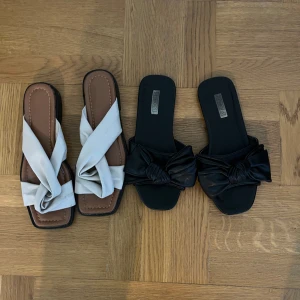 Två par slip-in sandaler med knutdetalj - Säljer två par trendiga slip-in sandaler med fyrkantig tå och knutdetalj framtill. Ett par är vita med brun sula och det andra paret är helsvarta. Perfekta för sommaren och lätta att matcha till olika outfits. 50kr styck