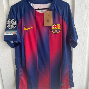 FC Barcelona Lamine Yamal matchtröja - Säljer en FC Barcelona matchtröja med Lamine Yamal och nummer 19 på ryggen. Tröjan är blå och röd med gula detaljer, klubbmärke på bröstet och Champions League-märke på ärmen. Kortärmad modell i lätt material.