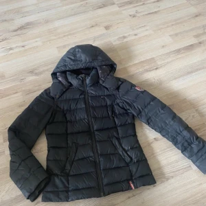 Svart dunjacka från Hilfiger Denim - Säljer en svart dunjacka från Tommy hillfiger med huva och dragkedja framtill. Jackan har quiltad design och två fickor med dragkedja. Perfekt för kyligare dagar och har en snygg, sportig look.