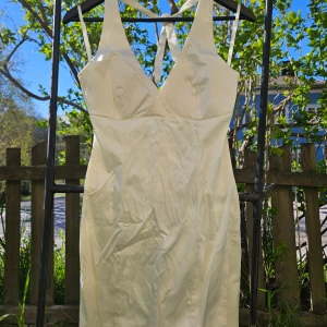 Vit långklänning med halterneck - Säljer en elegant vit långklänning med halterneck och djup urringning. Klänningen har en slät, figurnära siluett och knytning i nacken. Perfekt för speciella tillfällen. Skräddarsydd strl 36. Obs vikväck på bild, levereras nytvättad och struken.