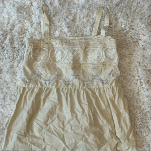 Beige spetsdetaljerad linnetopp från Zara - Säljer en söt beige linnetopp från Zara med vackra spetsdetaljer upptill. Toppen har axelband och ett vackert broderat mönster över bysten. Perfekt för varma dagar och enkel att matcha med jeans eller kjol. (Omgjord från klänning)