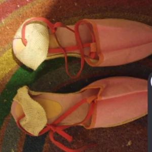 Rosa sandaler med snörning -  Unika rosa sandaler med röda snören och beige detaljer vid hälen, från Ilse Jacobsen. Skorna har en platt sula och öppen design, perfekta för varmare dagar. Färgglad och lekfull stil som sticker ut.