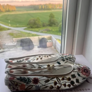 Blommiga ballerinaskor - Säljer ett par ballerinaskor med blommigt mönster i flera färger. Skorna har rund tå och är i tygmaterial, perfekta för vår och sommar. Superfina detaljer med broderade blommor som ger en unik look.
