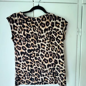 Leopardmönstrad topp från lager 156 - Säljer en snygg leopardmönstrad topp från lager 157 i storlek S. Toppen har korta ärmar och är tillverkad i ett mjukt, stretchigt material. Perfekt för dig som vill sticka ut med ett djurmönster! Har aldrig använt den och säljer för den just inte kommer till användning.
