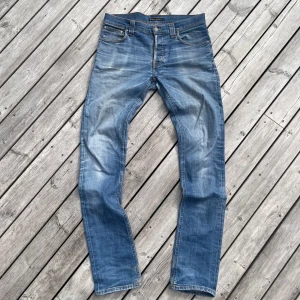 Blå jeans från Nudie Jeans - Säljer ett par klassiska blå jeans från Nudie Jeans med snygga slitningar och kontrastsömmar. Modellen har fem fickor och raka ben. Perfekta för dig som gillar en tidlös jeansstil. Skriv gärna vid funderingar🔥