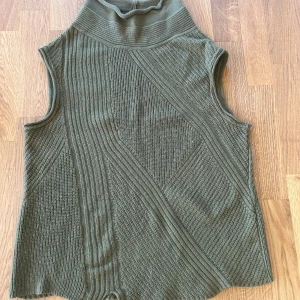 Olivgrön stickad ärmlös polotopp från Oska - Säljer en olivgrön stickad polotopp från Oska. Toppen är ärmlös med hög polokrage och har ett snyggt strukturerat mönster med olika stickade partier. Perfekt att styla lager på lager eller bära som den är.