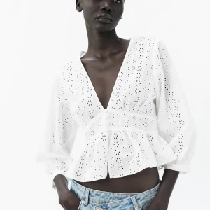Vit broderad blus med v-ringning - Säljer en söt vit blus med broderade hål och v-ringning. Blusen har trekvartsärmar, knappar framtill och en lätt volang nertill. Perfekt till jeans eller kjol för en fräsch look. Helt oanvänd med prislappen kvar! Nästan helt slutsåld och svårt att få tag i