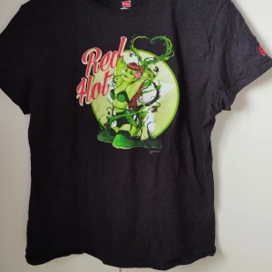 Pin-up Poison Ivy t-shirt - Cool svart t-shirt från Hanes med Poison Ivy-tryck och texten 'Red Hot' i rött och rosa. Det står stlm L men känns mer som M. T-shirten är i 100% bomull och har klassisk passform med korta ärmar. Perfekt för dig som gillar DC Comics och vill sticka ut med en färgstark print.