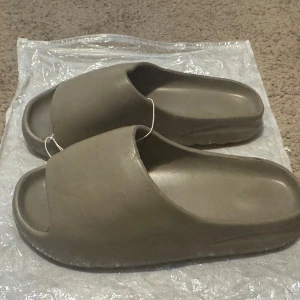 Nya tofflor Slides  - Nya tofflor i mörk beige.                         Storlek: 41-42                                                         Färg: mörk beige 