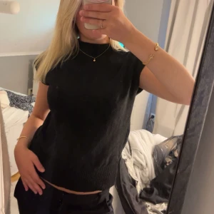 Svart stickad ärmlös tröja - Snygg svart stickad tröja med ribbad nederkant och ärmlös design. Perfekt att styla med jeans eller kjol för en clean look. Enkel och stilren.  