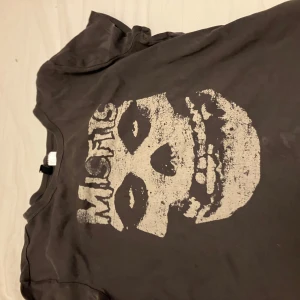 Svart Misfits t-shirt med tryck - Cool svart t-shirt från H&M med stort Misfits-tryck framtill. Klassisk rund hals och korta ärmar. Perfekt för dig som gillar bandmerch och vill ha en edgy vibe. Materialet är mjuk bomull som känns skönt mot huden.