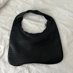 Svart axelväska i skinnimitation  - Säljer en svart axelväska i braided modell, med snyggt flätat mönster och dragkedja upptill. 