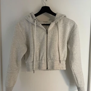 Lounge-hoodie - Säljer en ljusgrå croppad hoodie från Lounge som sitter otroligt snyggt i midjan. Passar lika bra över en kjol eller klänning som till jeans eller kostymbyxor. Plagget har inga defekter och är mycket sparsamt använd! 