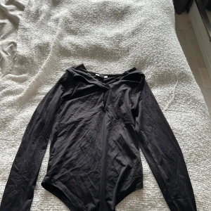 Svart långärmad body med snygg detalj - Säljer en svart, långärmad body med en detalj vid bröstet, endast använd ett fåtal gånger.