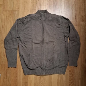 Beige fullzip - Snygg beige kofta från Daniel Hechter i storlek M. Tröjan har hel dragkedja, ribbad krage och detaljer vid axlar, ärmslut och nederkant. Perfekt för lager-på-lager och chillare dagar. Materialet är mjukt och stickat för extra komfort.