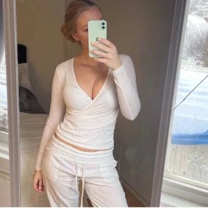 Vit omlottopp med v-ringning - Säljer en vit långärmad omlottopp med djup v-ringning. Toppen är ribbad och har en figurnära passform som framhäver siluetten. Perfekt att styla med både jeans och kjol för en trendig look sitter som xs/s.