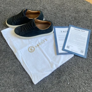 Svarta mockasneakers från Skolyx - Stilrena svarta sneakers från Skolyx i mocka med vita platta sulor och klassisk snörning. Insidan är fodrad i ljust skinn för extra komfort. Perfekta för dig som gillar minimalistisk och clean look. Köptes för 1699 förra vintern och är i bra skick! Skriv vid minsta fundering och ge prisförslag😄