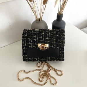 Svart axelväska, med nitar och rutigt tyg. - Snygg svart axelväska med rutigt tyg i svart och guld, guldfärgad trasig kedja som lätt går att byta ut som en annan och elegant låsdetalj framtill. 