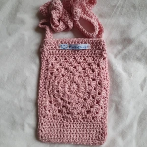 Rosa virkad axelväska från LindaDesign - Söt rosa axelväska från LindaDesign, handvirkad med ett dekorativt mönster framtill. Väskan har en lång axelrem och är perfekt för att bära småsaker. Liten och smidig modell som passar till många tillfällen.