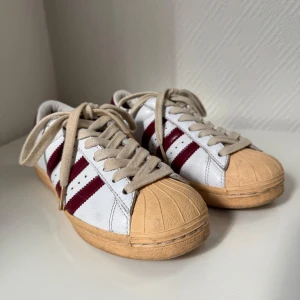 Adidas Superstar 38 - Säljer ett par Adidas Superstar i storlek 38.  Den har inge hål eller något fel på skorna, funkar jätte fint och är i färg Vit/ vinröd Tyvärr så har jag ingen orginal förpackning eller kvitto på skorna. Priset kan diskuteras och snabba leveranser 