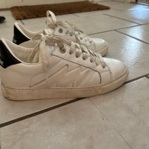 Vita sneakers från Zadig & Voltaire - Säljer ett par vita sneakers från Zadig & Voltaire med svarta detaljer på hälen. Skorna är använda endast under ett tillfälle, inga slitningar utan det är bara smuts som går att tvätta bort. Storlek 36 men passar mig som är från 36-37. Nypris 3000 mitt pris: 1900kr 