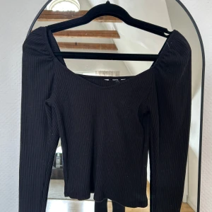 Svart ribbad långärmad topp - Säljer en svart ribbad långärmad topp med snygg v-ringning och figurnära passform. Perfekt att styla med jeans eller kjol för en clean look. Materialet är stretchigt och bekvämt, vilket gör den enkel att bära hela dagen. Från h&m