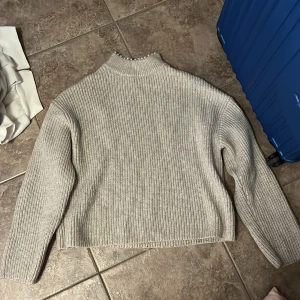 Beige stickad polotröja med pärlor H&M - Superfin beige stickad polotröja från H&M i ribbat material. Tröjan har långa ärmar och en hög krage som är dekorerad med pärlor runtom. Perfekt för dig som gillar en stilren look med en extra detalj.