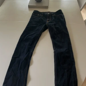 Mörkblå jeans från Nudie Jeans Co - Snygga mörkblå jeans från Nudie Jeans Co med klassiska orange sömmar och läderpatch bak. Jeansen har rak passform och är tillverkade i slitstarkt denim. Perfekta för dig som gillar stilrena och tidlösa jeans med schyssta detaljer.