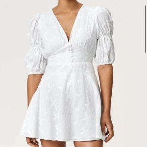 Vit adoore klänning med puffärm - Superfin vit kort adoore Sicily dress med broderade blommor, puffiga trekvartsärmar och v-ringning. Klänningen har knappar framtill och markerad midja som ger en snygg siluett. Perfekt för student eller sommarens alla tillfällen! Endast använd en gång 🙏🏻💕💕