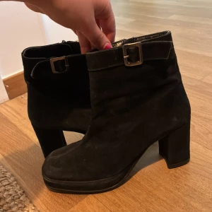 Vintage Tamaris svarta boots  - Säljer ett par ikoniska svarta boots från Tamaris med hög klack och dekorativt spänne vid ankeln. Min mamma har haft dessa sen 90-talet men nu är det dags att säga adjö!🥹 De har dragkedja på insidan och är tillverkade i mocka. 