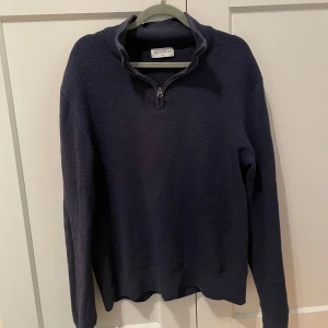 Mörkblå stickad tröja med halv dragkedja från These Glory Days - Säljer en stilren mörkblåa halfzip tröja från These Glory Days. Tröjan har en praktisk dragkedja vid halsen och är tillverkad i ett mjukt material. Perfekt för alla tillfällen, passar till allt. Den är köpt på Volt för 900kr. Mycket bra skick. Bara höra av sig vid frågor, priset kan diskuteras vid smidig affär!
