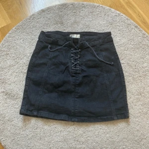 Svart jeanskjol med snörning - Svart kort jeanskjol från g perfect jeans med snygg snörning framtill i midjan. Kjolen har en lätt A-linjeform och är tillverkad i ett stadigt jeanstyg. Perfekt att styla med en enkel topp eller hoodie.