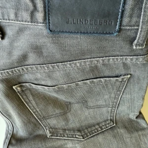 Grå jeans från J.Lindeberg - Snygga grå jeans från J.Lindeberg med klassisk femficksdesign och diskret JL-logo på myntfickan. Jeansen har normal passform och raka ben, tillverkade i mjukt bomullsjeansmaterial. Perfekta för en stilren och avslappnad look. W32/31 - L32