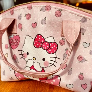 Söt liten väska med Hello Kitty-motiv! - Söt liten väska med handtag, dragkedja, justerbart axelband och Hello Kitty-motiv! Mått: 20 x 20 cm. Oanvänd.