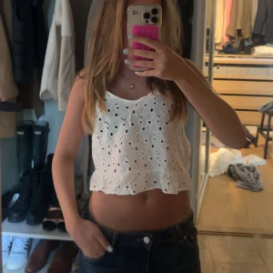 Vit broderad croppad linnetopp - Superfin vit croppad linnetopp med broderade hål och volangkant nertill. Den är från Hollister och är i strl M 